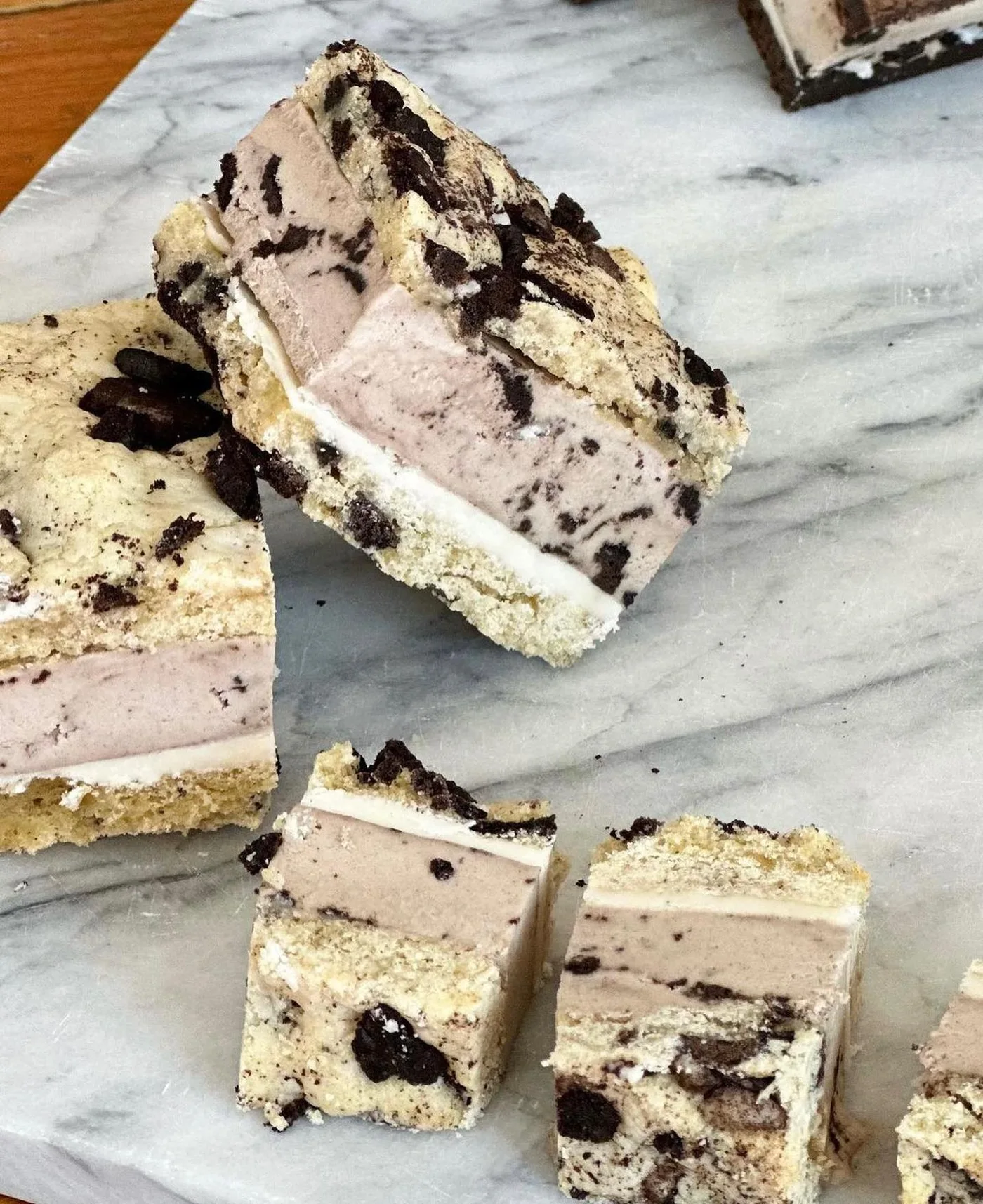 Cookies and cream ice cream bars cut into pieces on a marble board, showing their layers
